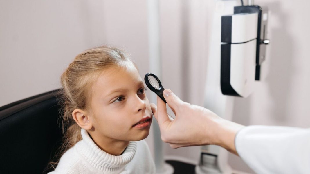 A young girl sitting in an ophthalmologist's office having her eyes examined.